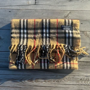 Rutig halsduk från Burberry - Säljer en klassisk rutig halsduk från Burberry i beige, svart och röd. Den har inga defekter och är nästan i nyskick. 145cm lång, 30cm bred. Skicka prisförslag om du är intresserad!
