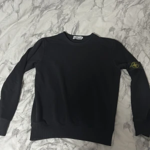 Svart tröja från Stone Island - Säljer en stilren svart tröja från Stone Island med deras ikoniska märke på ärmen. Tröjan har långa ärmar och en klassisk rund halsringning. Perfekt för en casual look. Kan gå ner i pris vid snabb affär 