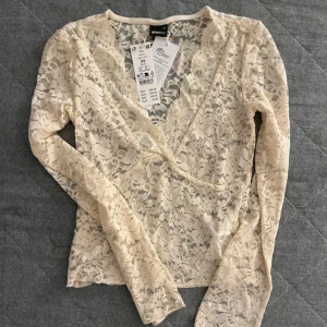 Vit spetsblus från Gina Tricot - Säljer en elegant vit spetsblus från Gina Tricot. Blusen har en v-ringad design med långa ärmar och ett vackert spetsmönster. Perfekt för att ge en romantisk touch till din outfit.