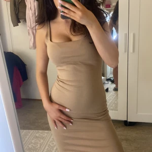 Beige tight klänning - Säljer en stilren beige klänning med smala axelband och tight passform. Perfekt för en elegant look. Klänningen är knälång och har en enkel design som framhäver figuren. Säljs inte längre