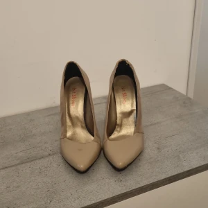 Beige pumps med spetsig tå - Snygga beige pumps med spetsig tå och klack. Perfekta för en elegant look. Skorna har en stilren design och är tillverkade i syntetmaterial.