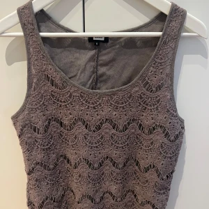 Beige ärmlös topp från Bik Bok stl S - Snygg beige ärmlös topp från Bik Bok med ett vågigt spetsmönster. Perfekt för att lägga till en touch av elegans till din outfit. Toppen har en rund halsringning och är i ett mjukt material.