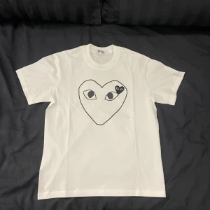 Comme des Garçons T-shirt - En riktig snygg vit T-shirt från Comme des Garçons. Med en svart logga på framsidan av tröjan på bröstet. Samt en broderad logga på  vänster sida av bröstet. | Den är så gott som ny i skicket 9,5/10. | Det är bara att höra av sig om man har några frågor🤍🤍🤍