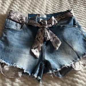 Blå jeansshorts från Monday - Snygga blå jeansshorts från Monday med fransiga kanter och ett coolt ormskinnsmönstrat bälte. Kostar 399 i butik 