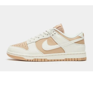Nike Dunk Low sneakers i beige och vit - Snygga Nike Dunk Low sneakers i en stilren kombination av beige och vit. Skorna har en klassisk design med snörning och rund tå, perfekt för en avslappnad stil.