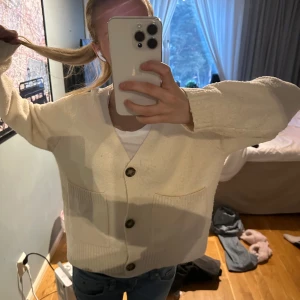 Vit kofta med knappar - Mysig vit kofta med stora knappar framtill. Den har en avslappnad passform och ribbade muddar vid ärmslut och nederkant. Perfekt för kyliga dagar.