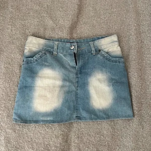 Kort Jeanskjol från Open Up - Trendig jeanskjol från Open Up i en kort modell med blekta detaljer. Kjolen har klassiska fem fickor och en knappstängning fram. Perfekt för en avslappnad stil.