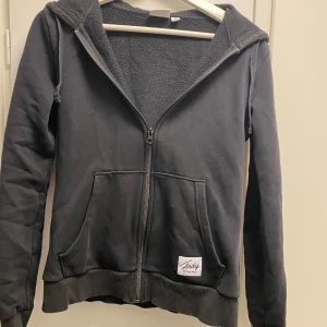 Svart hoodie från Andy by Frank Dandy - Säljer en svart hoodie från Andy by Frank Dandy. Den har en dragkedja framtill och en mysig insida. Perfekt för kyliga dagar. Huvan ger extra värme och stil. Passar bra till både jeans och joggers.