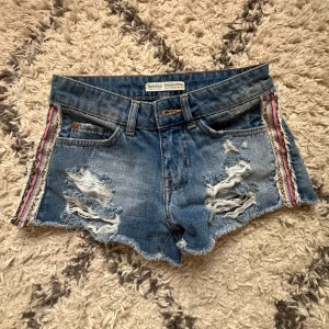 Blå jeansshorts från Bershka - Säljer jätte snygga blåa jeansshorts, de har slitna detaljer och färgglada mönster på sidorna💕💕