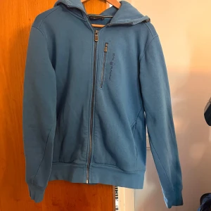Blå hoodie från Sail Racing - Fin ljusblå hoodie från sail racing. Tröjan har inga skador eller fläckar. Nypris 1500kr