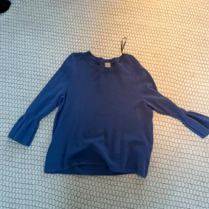 Blå tröja med volangärmar - Snygg blå tröja med unika volangdetaljer vid ärmsluten. Perfekt för att ge en stilren look med en twist. Tröjan har en rund hals och är tillverkad i ett mjukt material som känns skönt mot huden.