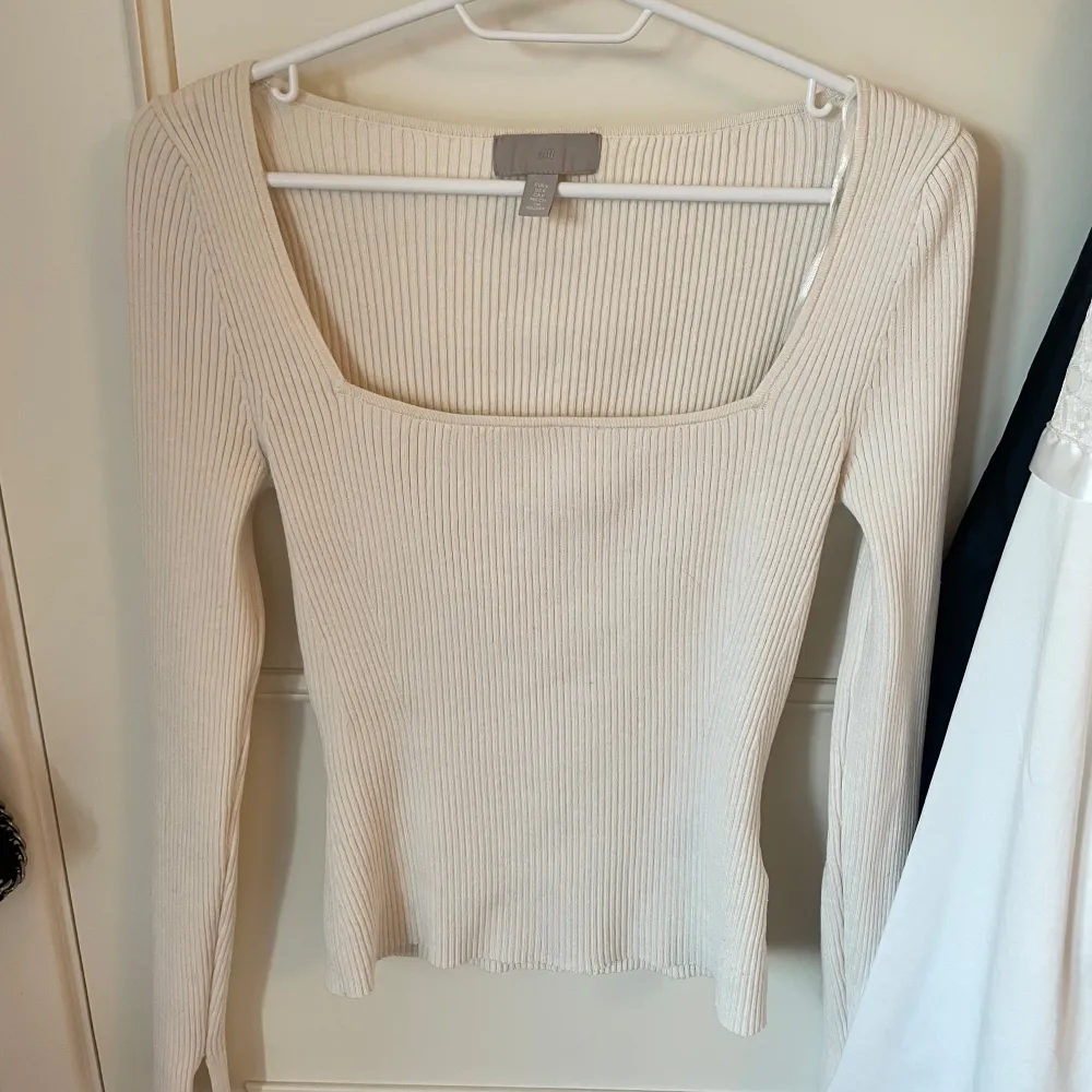 En beige ribbad tröja med lång ärm och fyrkantig halsringning. Toppen är från H&M i storlek S med slits i båda armarna. Neuletakit & Villapaidat.