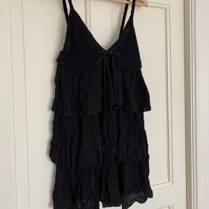Svart ärmlös klänning med volanger - Snygg svart klänning med volanger och en stickad överdel med knytning framtill. Endast använd en gång, fint skick!