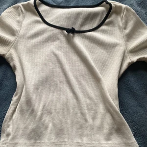 Vit ribbad topp med svart kant - Säljer en stilren vit  ribbad topp med korta ärmar och en svart kantdetalj vid halsringningen. Perfekt för en enkel och chic look.
