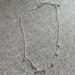 Silverfärgat halsband med små hängen - Elegant och stilrent silverfärgat halsband med små glittriga hängen. Perfekt för att lägga till en subtil touch av glamour till din outfit. Justerbar kedja för perfekt passform.Den är min mormors gammla.