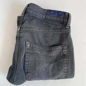 Grå dondupjeans - Snygga grå dondups med en klassisk design. Byxorna har en rak passform och är perfekta för en avslappnad stil. De har fickor både fram och bak samt en knapp- och dragkedjestängning.