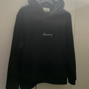 Svart hoodie från Saint Laurent - ✨Säljer en stilren svart hoodie från Saint Laurent med justerbar dragsko i huvan. Den har en diskret logotyp på bröstet och är tillverkad i Italien. Perfekt för en avslappnad och trendig look. Passar S-M Köpt här på Plick så har tyvärr inget kvitto. Tveka inte på att skriva om du undrar något! Pris inte hugget i sten!✨