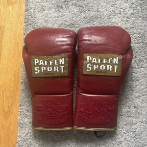 Röda boxningshandskar från Paffen Sport - Säljer ett par klassiska röda boxningshandskar från Paffen Sport med snörning och gulddetaljer. Handskarna är tillverkade i hög kvalitativt skinn och väger 10oz har tre lager av foam och är godkända för Professionell tävling dom är nästan helt nya har bara tästats så helt luktfria