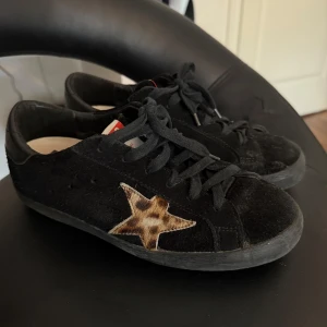 Golden Goose skor - Säljer ett par svarta sneakers från Golden Goose GGDB med en snygg leopardmönstrad stjärna på sidan. Skorna har svarta snören, svart sula och detaljer i skinn. Märket syns tydligt på baksidan. De är knappt slitna nånting alls. 