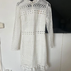 Vit spetsklänning från Two Sisters - Superfin vit klänning från Two Sisters med lång ärm och vackra spetsdetaljer. Klänningen har hög hals, dragkedja bak och ett genombrutet mönster som ger en unik look. Perfekt för bal,  skolavslutning eller bara att bära i sommar! 