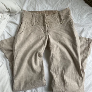 Beiga linnebyxor från Vero Moda - Säljer ett par så snygga beiga linnebyxor från Vero Moda. Byxorna har knappar framtill, hällor för bälte och sidfickor. Köpte dom av en annan tjej på plick men tyvärr va dom för små på mig på grund av att de är insydda i midjan på båda sidorna. Storleken är 38 men skulle säga att de passar en som har strl 34-36. Perfekta för varmare dagar och ger en avslappnad men stilren look.