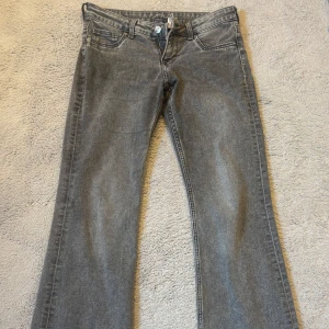 Grå bootcut jeans  - Säljer ett par grå jeans från h&m med bootcut-passform. Jeansen har klassisk femficksdesign, dragkedja och knapp framtill samt råa, slitna benslut för en cool look.