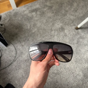 Svarta solglasögon från Tom Ford - Snygga svarta solglasögon från Tom Ford med bred båge och mörka linser. Glasögonen har en sportig och modern design med diskret gulddetalj på skalmen. Kommer med originalfodral och förpackning. Nypris 4600kr kvitto finns