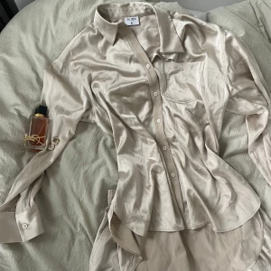 Beige satinskjorta-shortsset från Filippa K - Snyggt beige skjorta- och shortsset i satin från Filippa K. Skjortan har klassisk krage, lång ärm och bröstficka. Den har en glansig finish och knäpps framtill med knappar. Perfekt för en stilren och trendig look. Skulle vara perfekt för en solig och stilig dag på en varm uteservering!💘 Nypris ca 4000 kr. Aldrig använd!