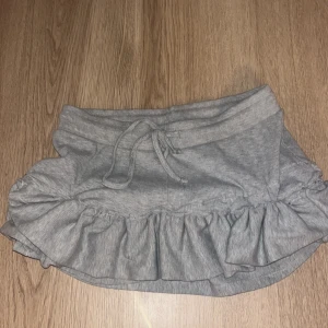 Grå volangkjol med knytband - Supersöt grå kjol med volangkant och knytband i midjan. Perfekt för en chill och avslappnad stil. Mjuk och bekväm, passar till många olika outfits.