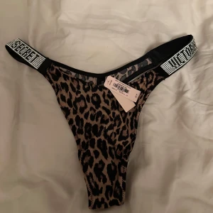 Leopardmönstrad trosa med strassdetaljer - Säljer en snygg leopardmönstrad trosa med breda svarta band och strassdetaljer på sidorna. Trosan har en hög skärning och är tillverkad i ett stretchigt material för bästa passform.