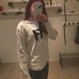 Vit stickad tröja med svart text - Säljer en vit stickad tröja med svarta bokstäver 'HT' på bröstet. Tröjan har rund halsringning och långa ärmar. Perfekt för dig som gillar enkel och stilren design. 