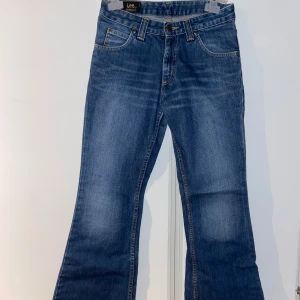Blå bootcut jeans från Lee - Säljer ett par klassiska blå jeans från Lee med bootcut-passform. Omkretsen på jeansens midja är ca 74 cm och längden på hela byxbenet är 100 cm.
