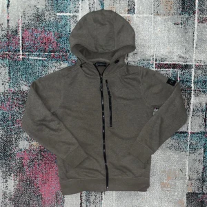 En härlig tröja med dragkedja från lagency -  hel dragkedja och huva från Lagency. Jackan har en bröstficka med dragkedja och en liten svart logotyp på ärmen. Perfekt för en avslappnad stil.