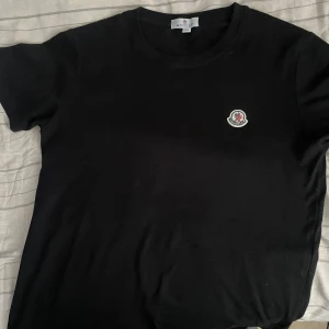 Svart t-shirt från Moncler - Säljer en svart t-shirt från Moncler med rund hals och klassisk passform. T-shirten har Moncler-logga broderad på bröstet och är tillverkad i mjuk bomull. Perfekt för en stilren och enkel look. Aldrig använt på grund av att den är liten på mig. Storlek M men passar S bättre 