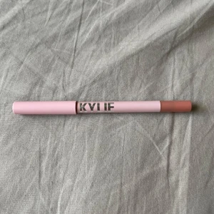 Kylie Jenner Läppenna - Säljer en Kylie Jenner läppenna i färgen 800 One Wish. Pennan har en mjuk, nude-rosa ton och kommer i en snygg ljusrosa hylsa med silvrig text. Perfekt för att definiera läpparna och skapa en naturlig look.