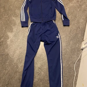 Adidas SST Primeblue tracksuit - Säljer ett par klassiska Adidas SST Primeblue tracksuit med vita ränder längs sidorna och broderad logga på låret och bröstet. Perfekta för träning eller en sportig look. Tröjan är i väldigt bra skick, medans byxorna är i ganska bra skick.
