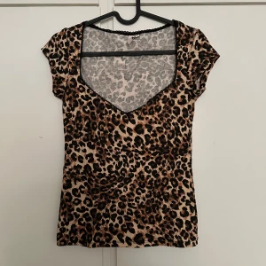 Leopardmönstrad topp med v-ringning - Säljer en snygg leopardmönstrad topp med v-ringning och korta ärmar. Toppen har en figurnära passform och är perfekt för dig som vill sticka ut lite extra. Mjuk och skön mot huden.