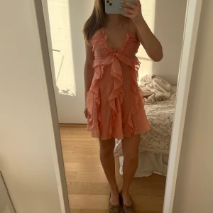  volangklänning - Säljer en söt aprikos färgad miniklänning med volanger. Klänningen har några miniatyr hål framtill men ingenting som märks på långt håll och knappt nära!! Köpt för 690kr 