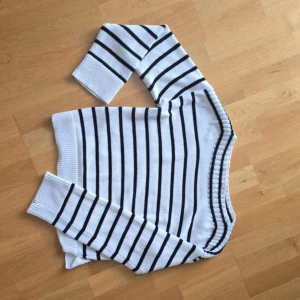 Vit och svart randig stickad tröja från AWARE - Säljer en vit stickad tröja med svarta horisontella ränder från AWARE. Tröjan har långa ärmar, bred ribbad mudd vid ärmslut och nederkant samt en klassisk rund halsringning. Perfekt för en stilren och avslappnad look.