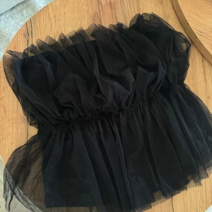 Svart tubtopp i tyll från Vero Moda - Säljer en svart tubtopp från Vero Moda i tyll. Toppen har resår i midjan för en snygg passform. Aldrig använd med prislapp kvar!