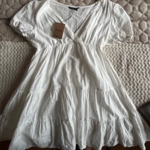 Vit kortklänning med v-ringning från Shein - Superfin vit klänning från Soaked in Luxury med v-ringning och puffärmar. Klänningen har volanger i kjolen och är tillverkad i ett lätt linnematerial. Perfekt för sommarens alla tillfällen! (Har en liten smink fläck i mitten som troligtvis går att tvätta bort)