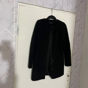 Svart kappa från ONLY - Säljer en stilren svart kappa från ONLY i storlek XS. Jackan har lång ärm, knäppning framtill och en klassisk rak passform. Perfekt för dig som gillar en enkel och tidlös look.