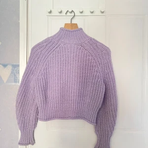 Ljuslila stickad polotröja - Säljer en supermysig ljuslila stickad polotröja med grov ribbstickning. Tröjan har lång ärm, hög krage och en något croppad passform. Perfekt för lager-på-lager och att hålla sig varm under kyliga dagar.