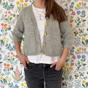 Grå trekvartärmad kofta med gula knappar - Säljer en superfin grå stickad kofta med trekvartsärmar och gulliga gula knappar. Perfekt för både vår och höst när det är lite kyligt. Den är croppad och har en mysig, loose passform. Passar perfekt över en t-shirt eller blus för en avslappnad look. Köpt second hand och misstänker att den är hemstickad. Står ingen storlek men jag brukar ha 36/38 som referens🙌🏼den är lite nopprig