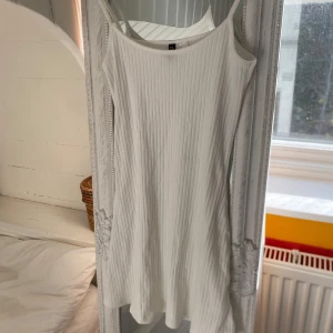 Vit ribbad klänning från h&m - Säljer en vit ribbad klänning från Divided i storlek XS. Klänningen har smala axelband och är ärmlös med en rak, enkel passform. Perfekt för varma dagar och enkel att styla med accessoarer.
