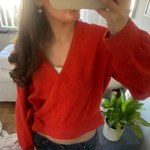 Röd omlottopp i stickat material - Säljer en röd croppad omlottopp i stickat material. Tröjan har långa ärmar och knyt i sidan, perfekt för dig som vill ha en trendig och bekväm look. St L men passar M också 