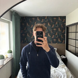 Polo Ralph Lauren Zip Tröja - Säljer en mörkblå hoodie från Polo Ralph Lauren med dragkedja och huva. Tröjan har två fickor framtill och en broderad vit logga på bröstet. Perfekt för en avslappnad stil. 