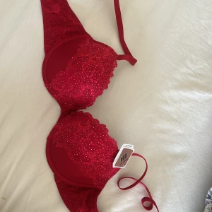 Röd push-up bh med spets och strass - Säljer en röd push-up bh med  spets och små strassdetaljer på kuporna. Bh:n har justerbara axelband och knäppe bak.  Original pris 250 men går att diskutera.