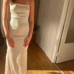 Champagnefärgad långklänning med smala axelband - Säljer en elegant långklänning i champagnefärg, rosa vit  med smala axelband och figurnära passform. Klänningen har öppen rygg. Den är från Nelly och säljs inte längre. Nypris 900kr💕storlek 34, jag bär vanligtvis S!!🥰