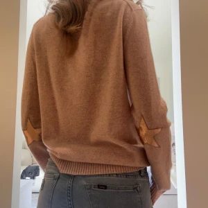Beige stickad tröja med stjärndetaljer - Mysig rosa/beige stickad tröja med lång ärm och ribbade muddar. Unik detalj med stjärnor i mocka på armbågarna. Perfekt för kyligare dagar och enkel att matcha med jeans. Köpte på Zadig och är aldrig använd